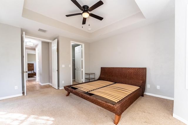 carpeted bedroom with a tray ceiling, visible vents, a ceiling fan, and baseboards