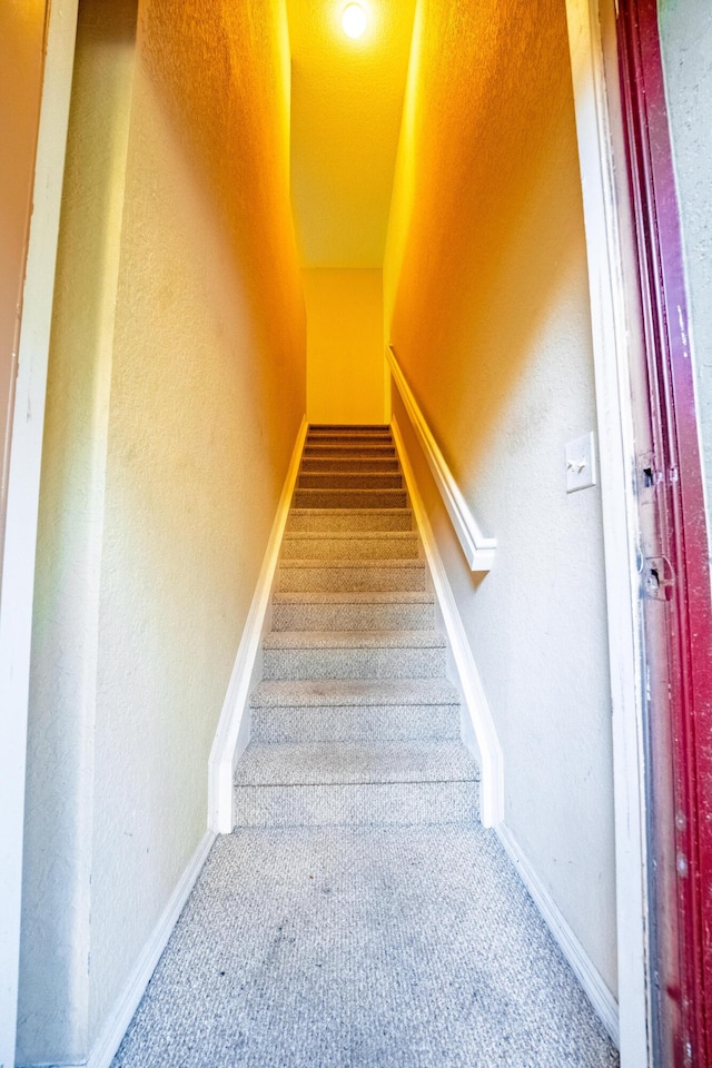 stairs with a textured wall, baseboards, and carpet floors