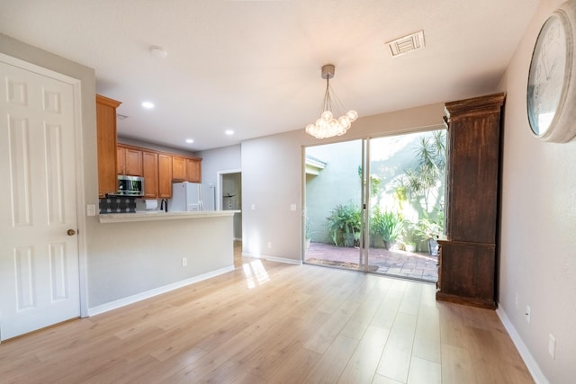 kitchen featuring an inviting chandelier, light wood-type flooring, kitchen peninsula, pendant lighting, and white refrigerator with ice dispenser