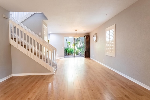 interior space featuring stairway, baseboards, a notable chandelier, and light wood-type flooring