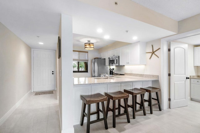 kitchen with appliances with stainless steel finishes, a kitchen breakfast bar, kitchen peninsula, light stone countertops, and white cabinets