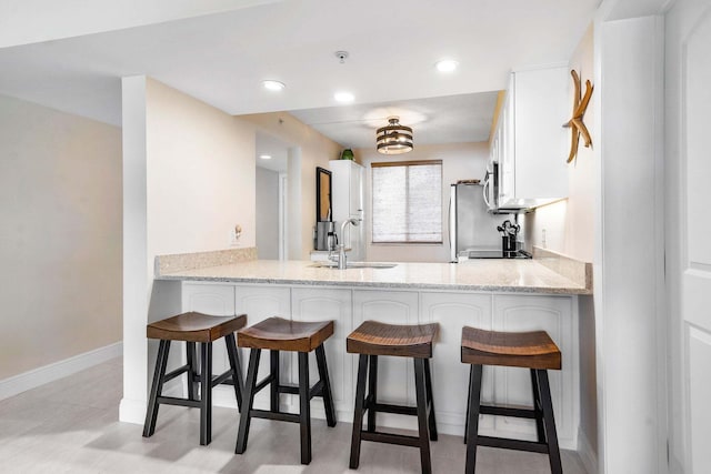 kitchen with light stone counters, kitchen peninsula, sink, and white cabinets