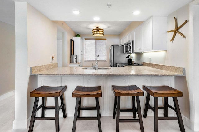 kitchen with sink, white cabinetry, stainless steel appliances, light stone counters, and kitchen peninsula