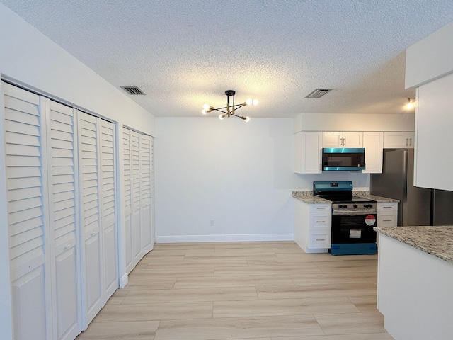 kitchen featuring white cabinets, a notable chandelier, light stone counters, stainless steel appliances, and light hardwood / wood-style flooring