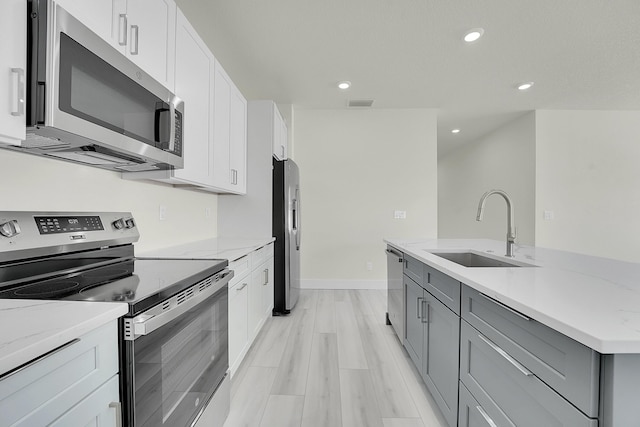 kitchen featuring sink, gray cabinetry, white cabinets, light stone counters, and stainless steel appliances