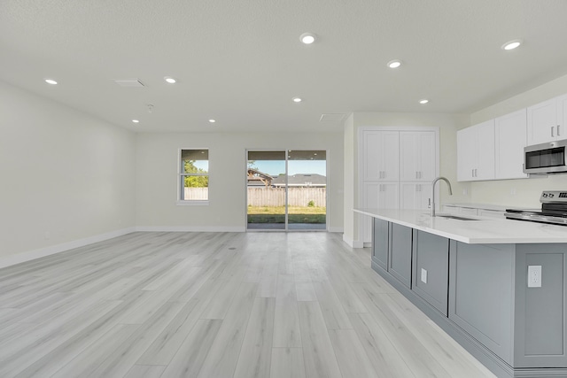 kitchen with sink, white cabinetry, light wood-type flooring, an island with sink, and stainless steel appliances