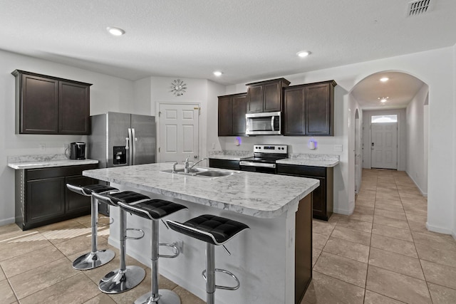 kitchen with arched walkways, appliances with stainless steel finishes, light countertops, dark brown cabinets, and a sink