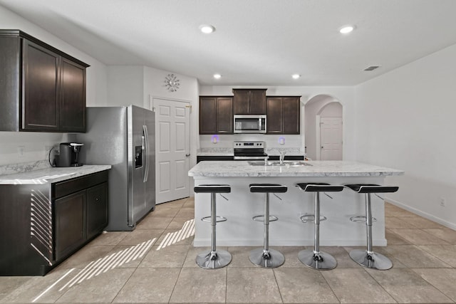 kitchen featuring arched walkways, a breakfast bar, stainless steel appliances, a sink, and dark brown cabinets