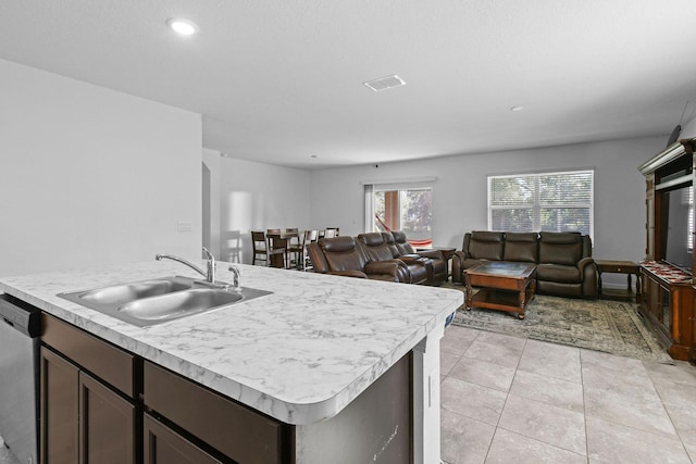 kitchen with light tile patterned floors, a kitchen island with sink, a sink, light countertops, and dishwasher