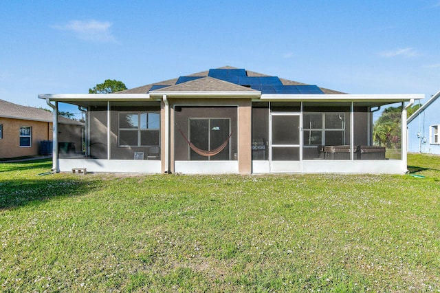 rear view of property featuring a sunroom, a yard, and roof mounted solar panels