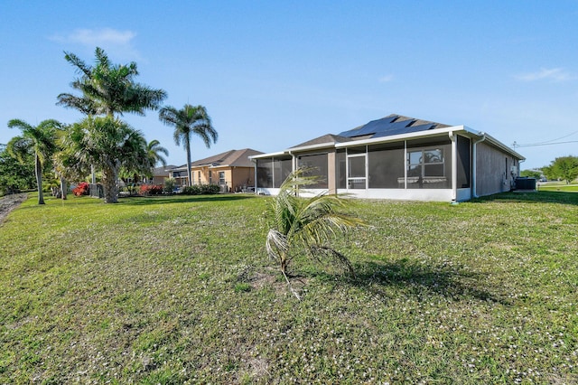 rear view of house with solar panels, a lawn, cooling unit, and a sunroom