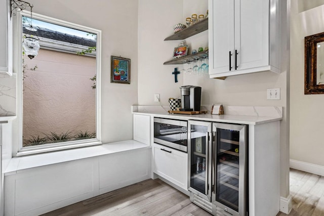 bar with beverage cooler, white cabinets, and light wood-type flooring