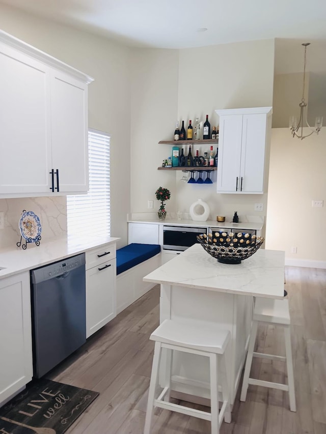 kitchen featuring pendant lighting, dishwasher, white cabinets, light stone counters, and light wood-type flooring