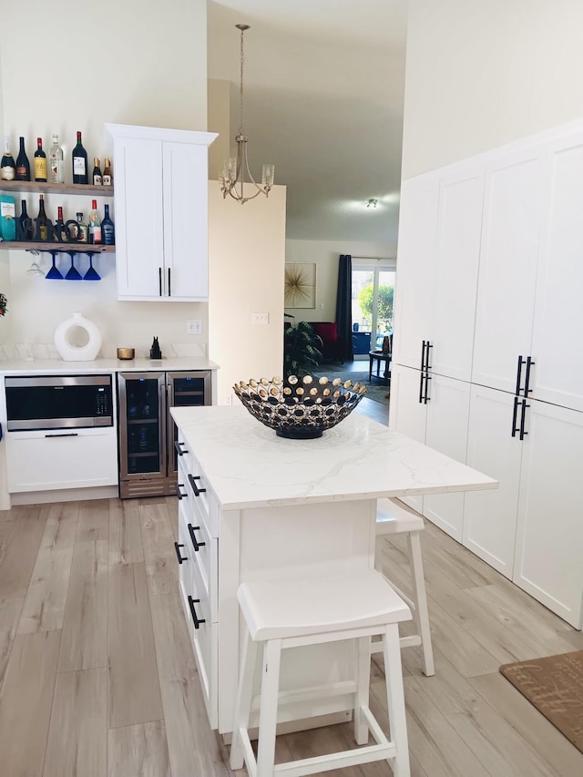 kitchen featuring light stone counters, decorative light fixtures, white cabinetry, and a breakfast bar