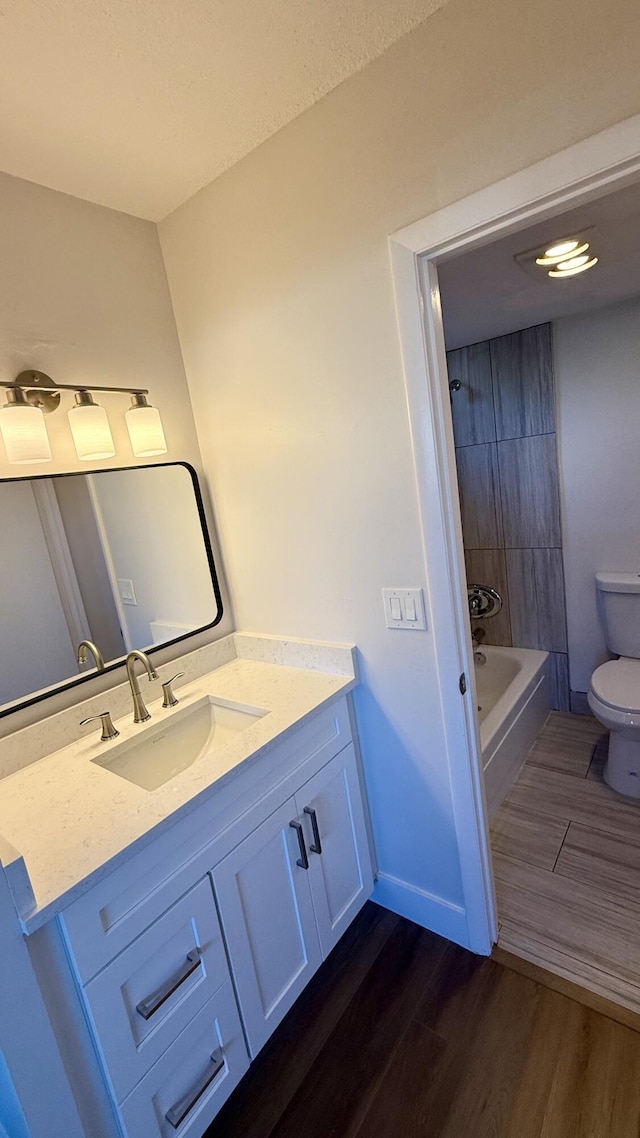 full bathroom featuring hardwood / wood-style flooring, vanity, toilet, and tiled shower / bath combo