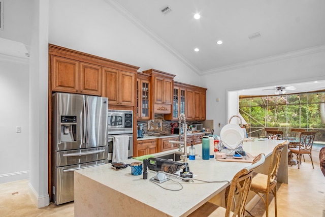 kitchen with crown molding, stainless steel appliances, tasteful backsplash, an island with sink, and vaulted ceiling