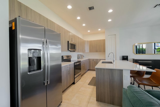 kitchen with sink, appliances with stainless steel finishes, a kitchen island with sink, a kitchen breakfast bar, and light tile patterned flooring