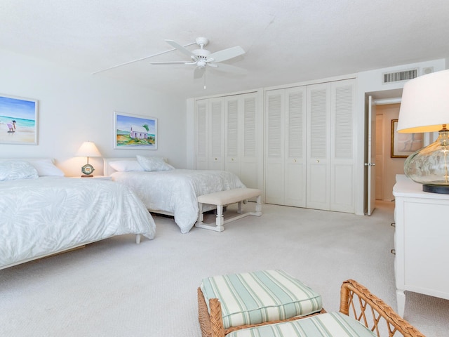 bedroom featuring two closets, light colored carpet, and ceiling fan