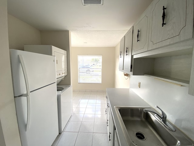 kitchen with white refrigerator, stacked washer / dryer, light tile patterned flooring, and white cabinets