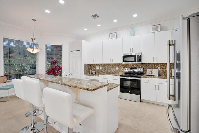 kitchen with hanging light fixtures, appliances with stainless steel finishes, a center island with sink, and white cabinets