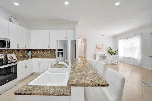 kitchen featuring crown molding, appliances with stainless steel finishes, white cabinets, a center island with sink, and decorative backsplash