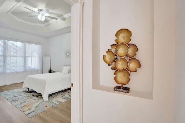 bedroom featuring ceiling fan, a raised ceiling, and light hardwood / wood-style floors