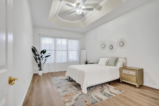 bedroom featuring crown molding, light hardwood / wood-style flooring, a raised ceiling, and ceiling fan