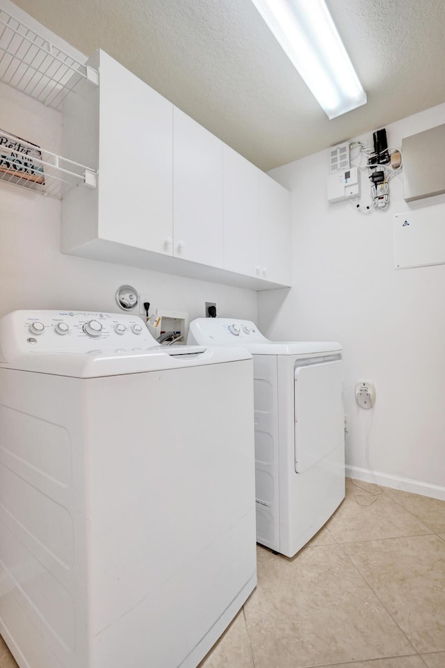 clothes washing area featuring cabinets, washing machine and dryer, light tile patterned floors, and a textured ceiling