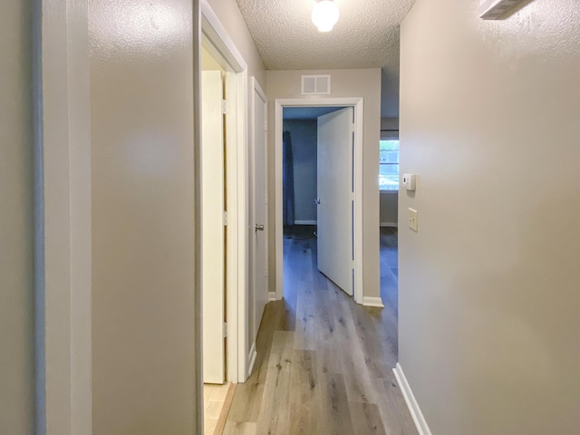 corridor with light hardwood / wood-style floors and a textured ceiling