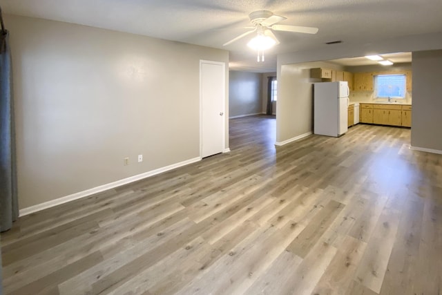 unfurnished living room with ceiling fan, sink, and light hardwood / wood-style flooring