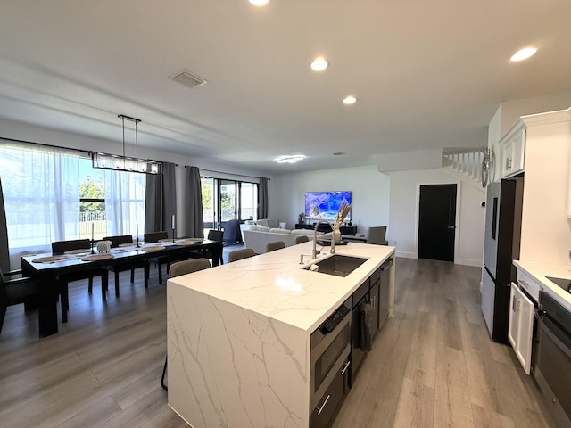 kitchen with decorative light fixtures, white cabinetry, sink, stainless steel fridge, and a center island with sink