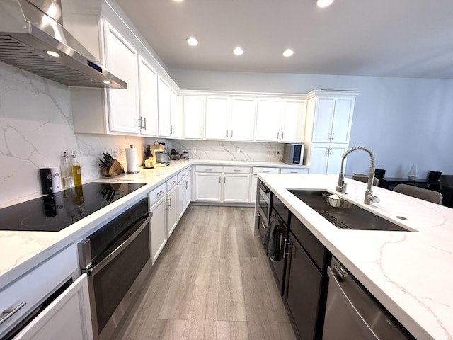 kitchen featuring wall chimney exhaust hood, sink, white cabinetry, appliances with stainless steel finishes, and light stone countertops