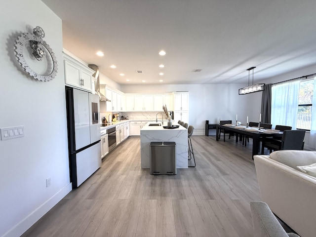 kitchen featuring fridge with ice dispenser, white cabinetry, stainless steel oven, hanging light fixtures, and a center island with sink