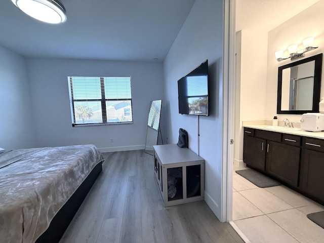 bedroom with connected bathroom, sink, and light wood-type flooring