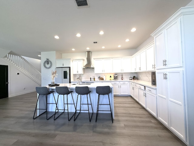 kitchen featuring wall chimney exhaust hood, tasteful backsplash, stainless steel refrigerator, a kitchen breakfast bar, and white cabinets