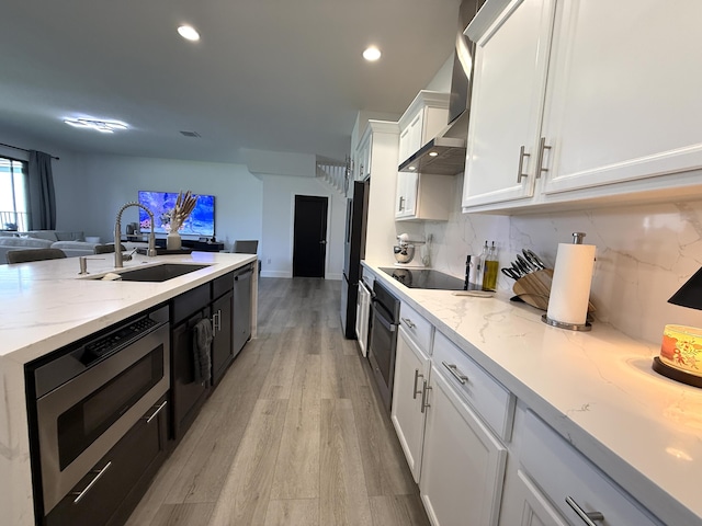 kitchen featuring appliances with stainless steel finishes, sink, white cabinets, decorative backsplash, and wall chimney range hood