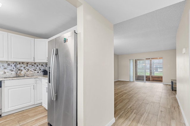 kitchen featuring sink, backsplash, white cabinets, light stone counters, and stainless steel fridge with ice dispenser