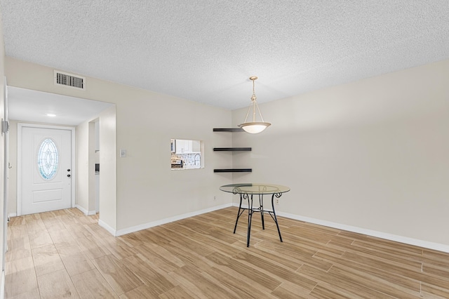 unfurnished dining area featuring a textured ceiling and light wood-type flooring