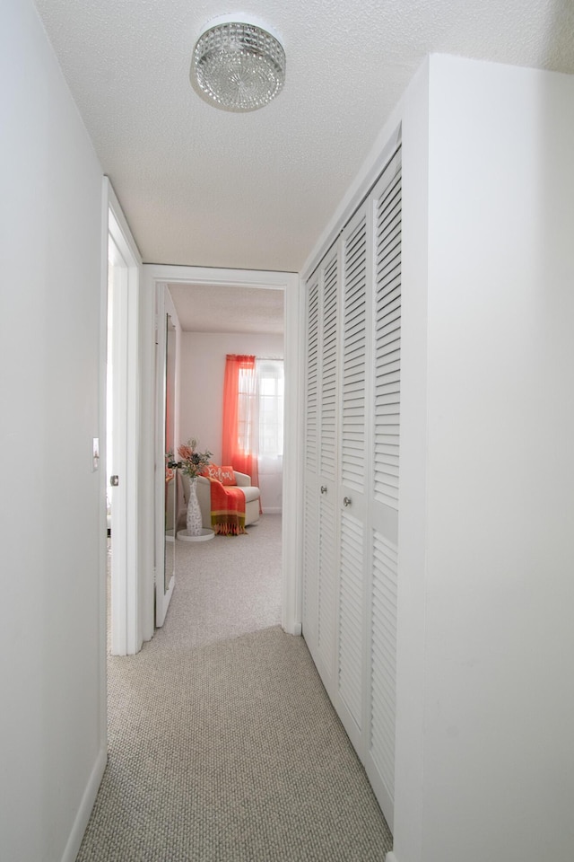 hallway with light carpet and a textured ceiling