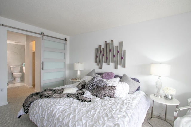 bedroom featuring ensuite bath, a barn door, and a textured ceiling