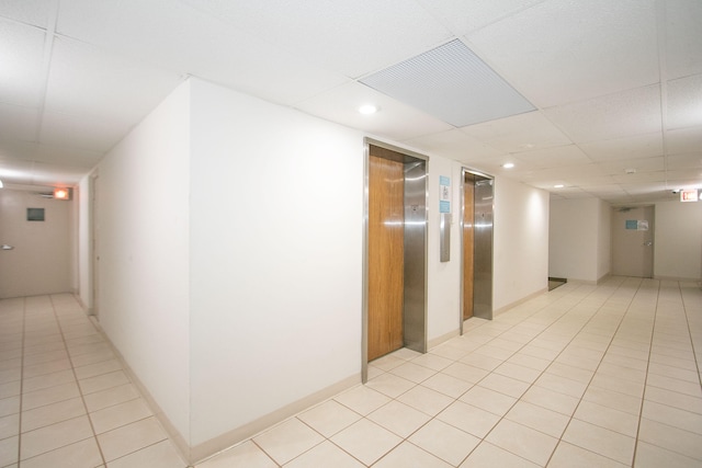 corridor with a paneled ceiling, elevator, and light tile patterned flooring