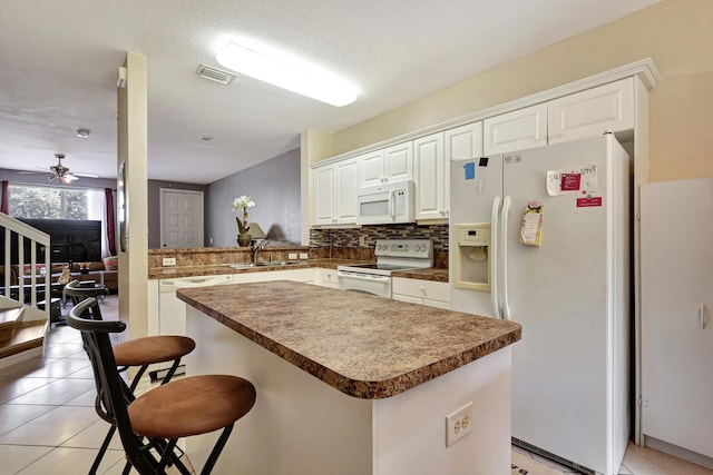 kitchen featuring a breakfast bar area, white cabinets, light tile patterned floors, kitchen peninsula, and white appliances