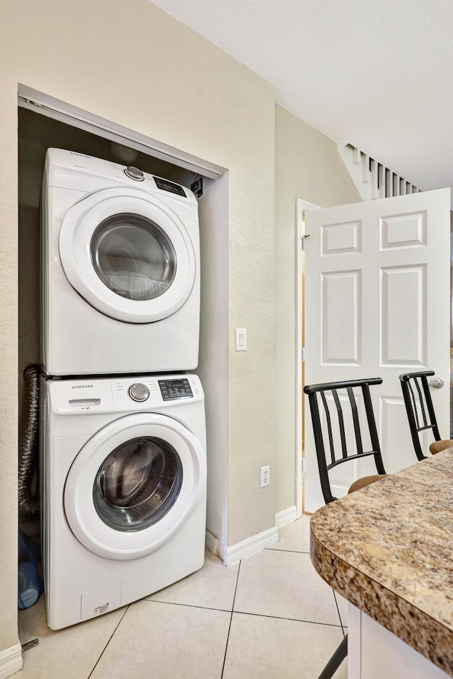 clothes washing area with light tile patterned flooring and stacked washer and dryer