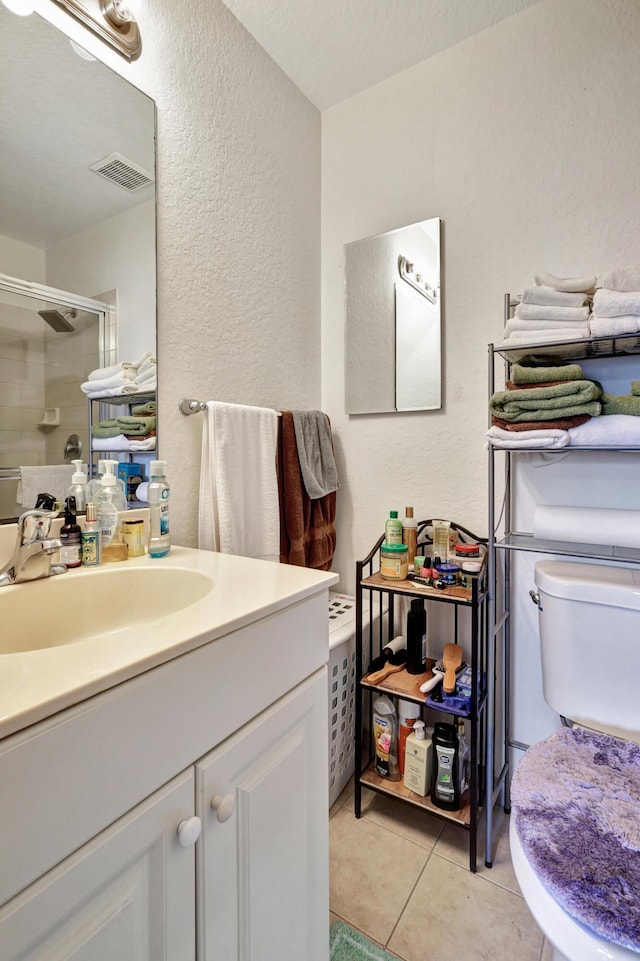 bathroom with tile patterned floors, toilet, a textured ceiling, vanity, and a shower with door