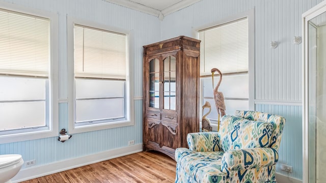 living area with wood finished floors, crown molding, baseboards, and wallpapered walls