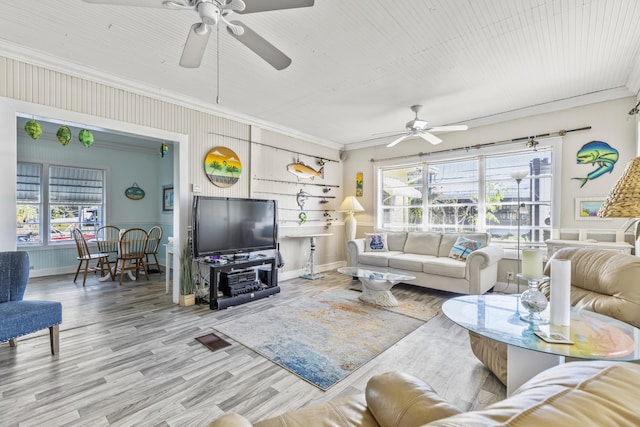living room with a ceiling fan, ornamental molding, healthy amount of natural light, wood finished floors, and baseboards