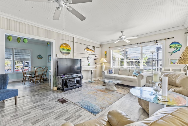 living room featuring ceiling fan, wood-type flooring, ornamental molding, and a healthy amount of sunlight