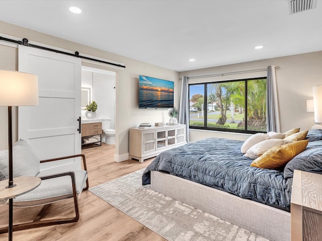 bedroom featuring ensuite bathroom, a barn door, and light hardwood / wood-style floors