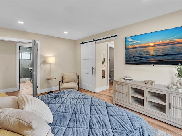 bedroom with ensuite bath, a barn door, and light hardwood / wood-style floors