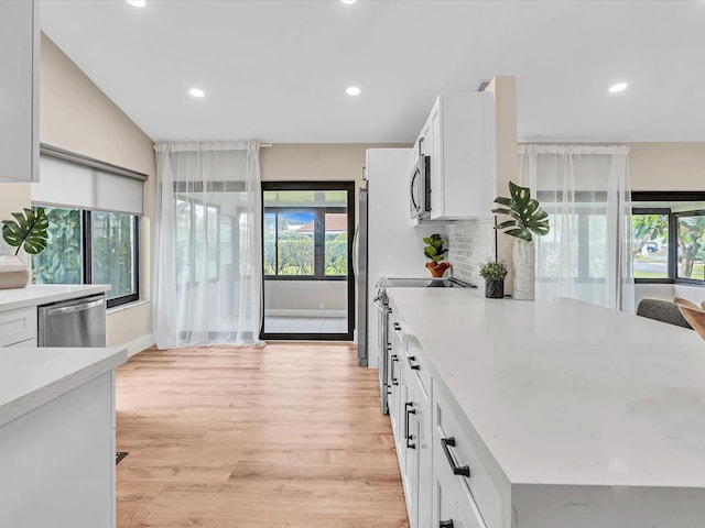 kitchen featuring stainless steel appliances, white cabinetry, tasteful backsplash, and light hardwood / wood-style floors